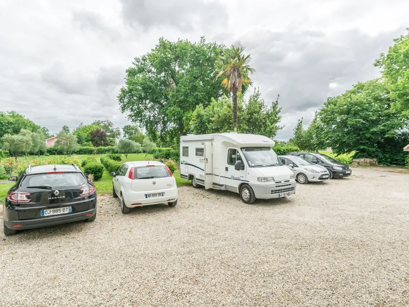 Motorhomes and cars parked at Château Beau Rivage in Bordeaux, surrounded by green trees under a cloudy sky