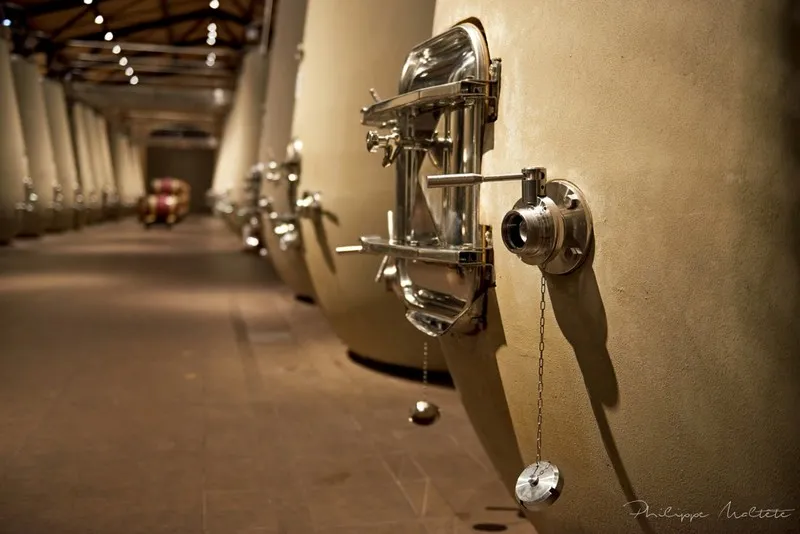 Row of stainless steel fermentation tanks lined along a corridor at Château Kirwan in Bordeaux, with control taps and suspension chains visible.