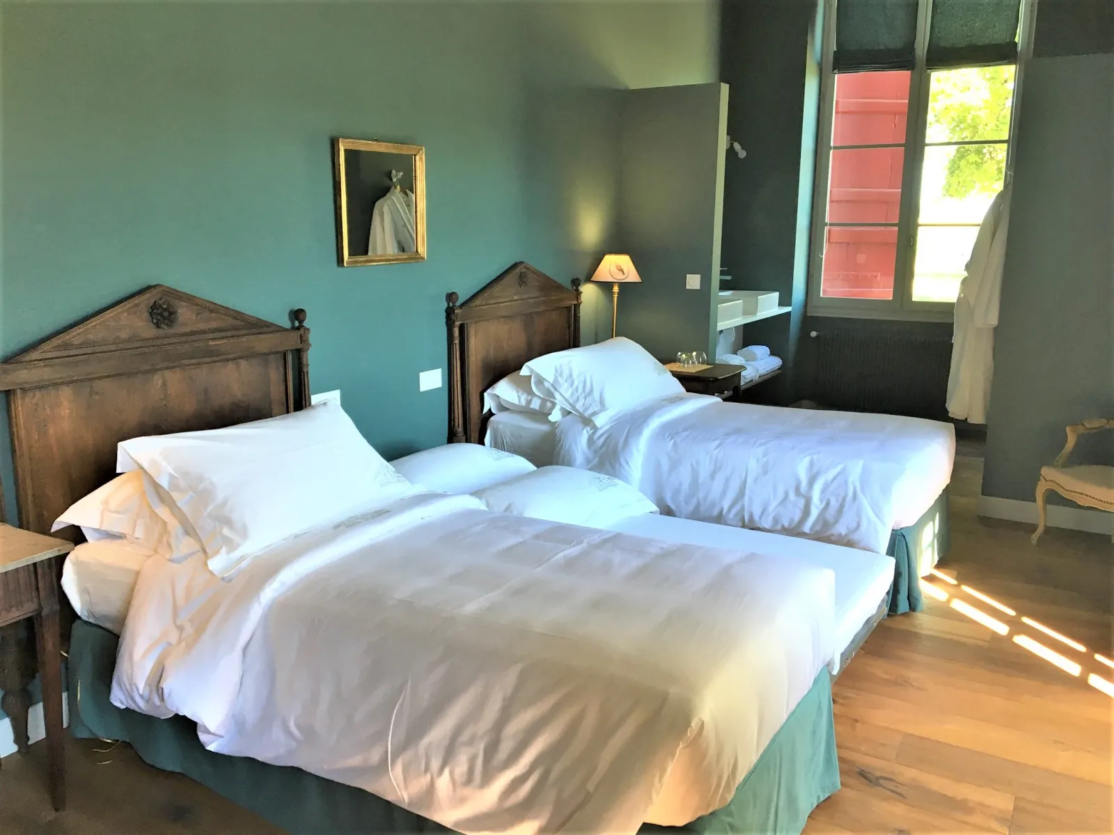 Elegant bedroom at Château Sigalas Rabaud in Bordeaux featuring two twin beds with white linens, turquoise and gray walls, antique wooden furniture, French doors opening to the garden, and refined décor