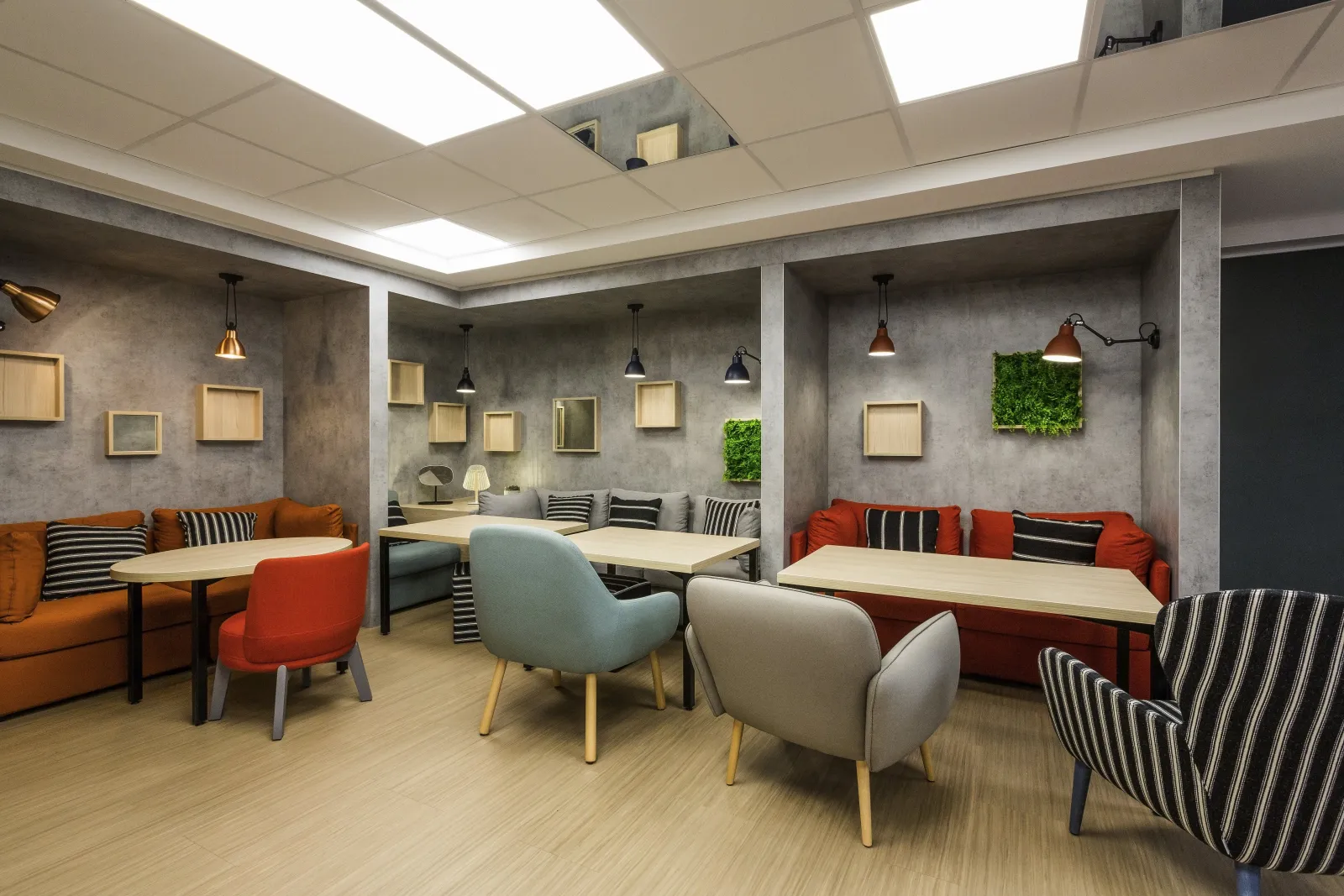 Modern coworking space at Ibis Bordeaux Centre featuring exposed concrete walls, orange and grey seating, white tables, LED lighting and green wall plants