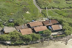 Aerial view of oyster parks with terracotta wooden cabins lined up in the Arcachon Basin, surrounded by green vegetation and water.