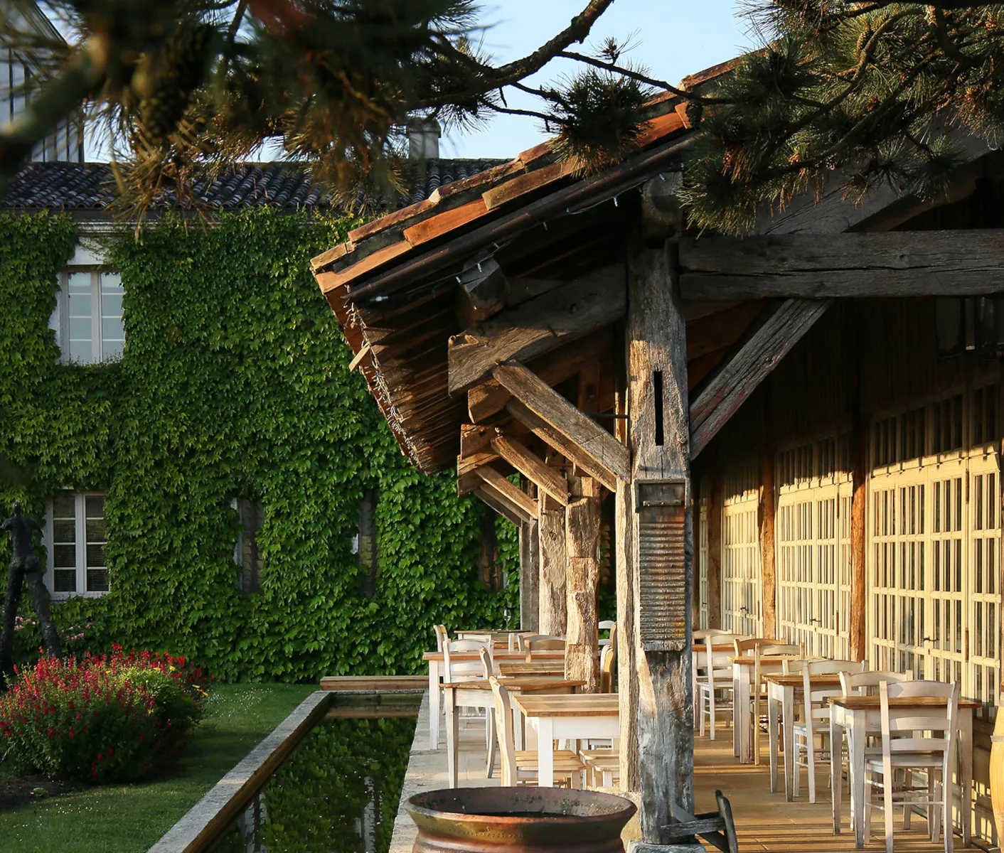 Wooden covered terrace of La Table du Lavoir in Bordeaux, featuring wooden chairs, ivy-covered building, and rustic pergola structure