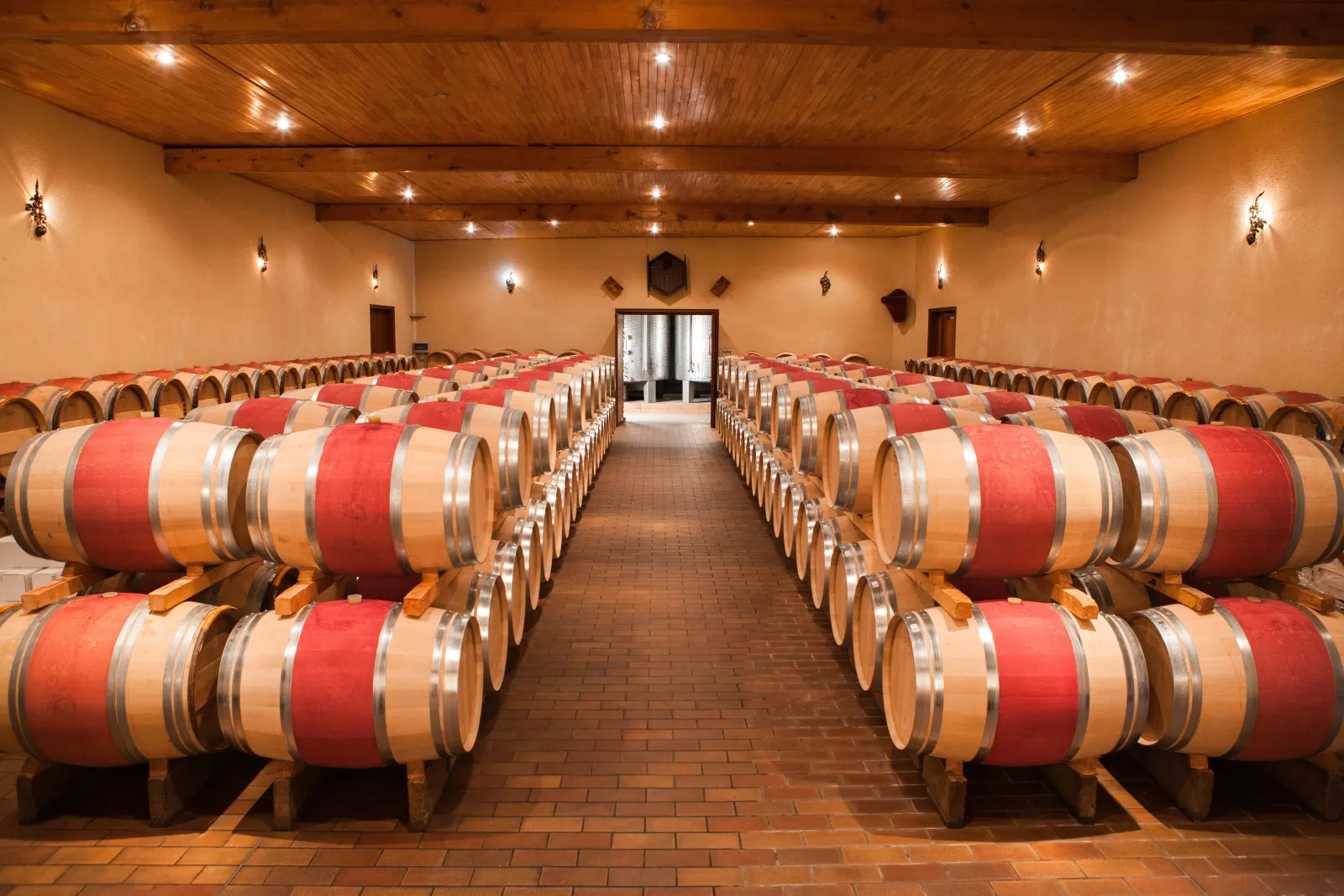 Wine cellar of Château Cap Léon Veyrin in Bordeaux featuring rows of oak barrels with red and beige bands, symmetrically arranged under a wooden ceiling with modern lighting.