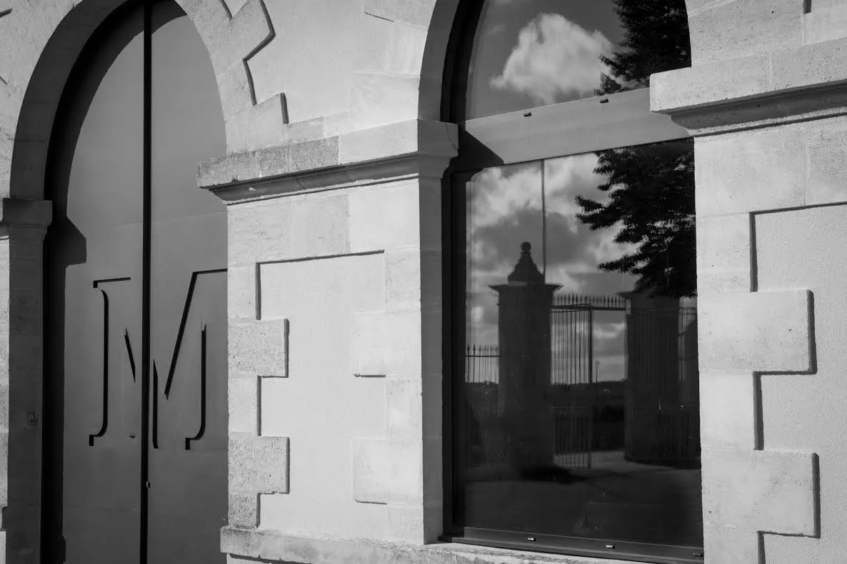 Black and white view of Château Malescasse in Bordeaux, featuring a stone arch, a glass window reflecting the castle's turrets, and geometric architectural details.