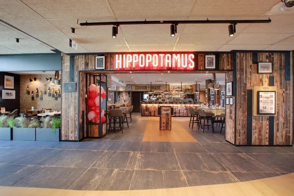 Hippopotamus restaurant storefront in Bordeaux featuring a red neon sign, light wooden facade with glass entrance, located in a modern shopping center.