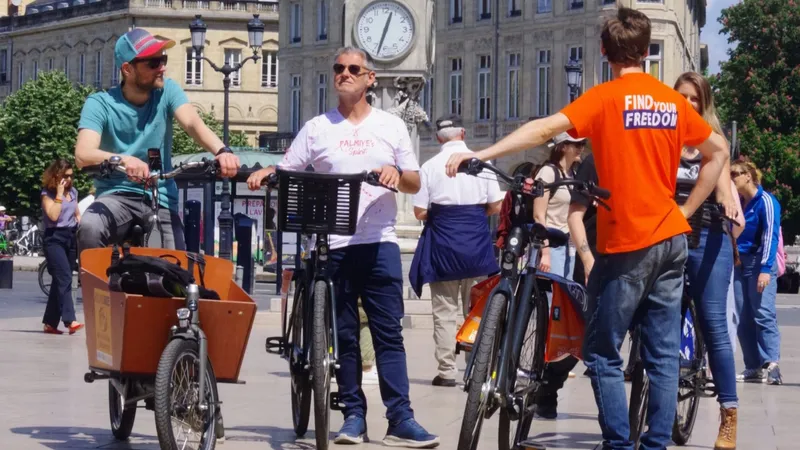 Group of cyclists with Holland Bikes rental bicycles posing on a square in Bordeaux, with a historic building and clock tower in the background.