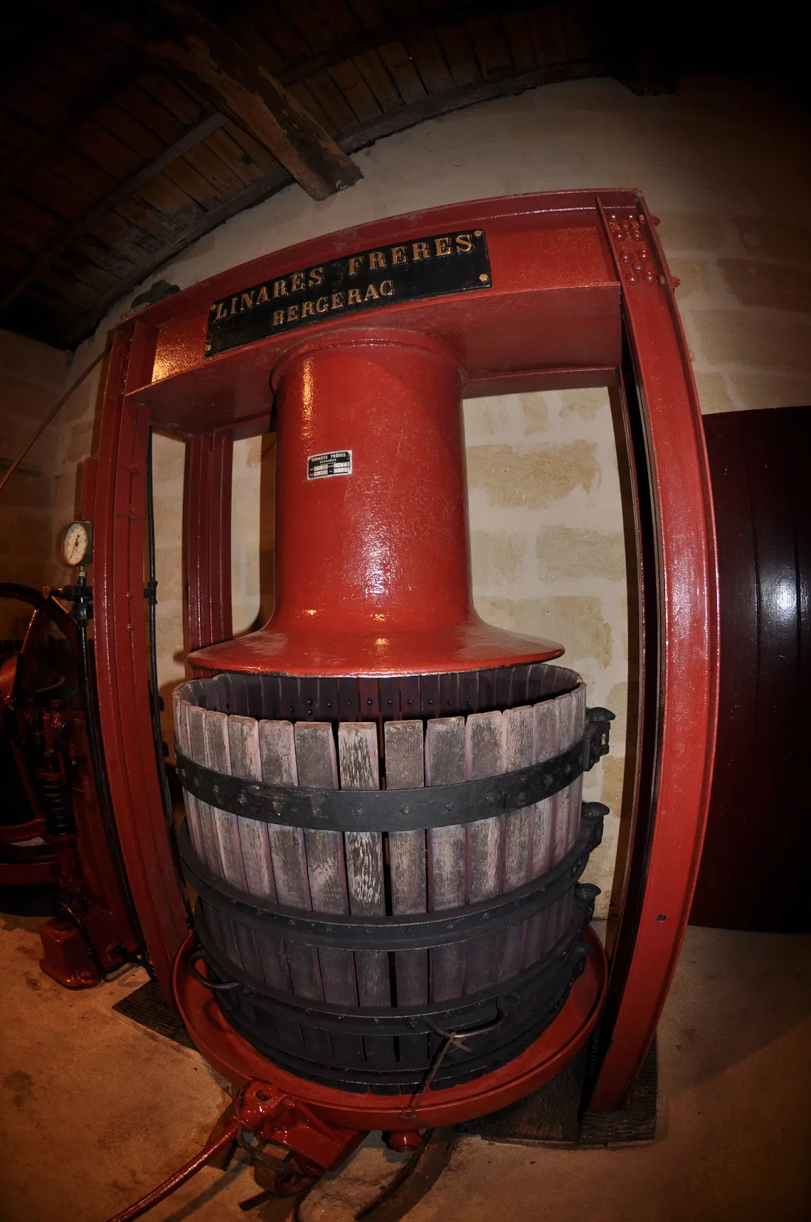 Historic red wine press from Château Laniote in Bordeaux, featuring traditional pressing mechanism and wooden barrels