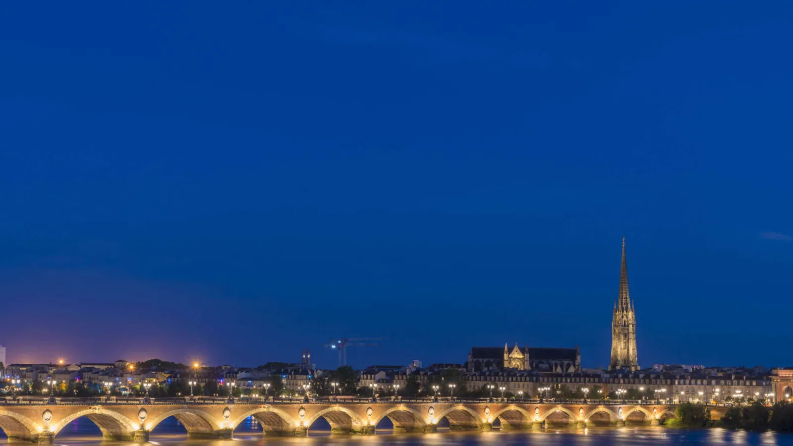 Night view of Bordeaux's Stone Bridge lit up with Saint-Michel Cathedral in the background and the Garonne River in the foreground