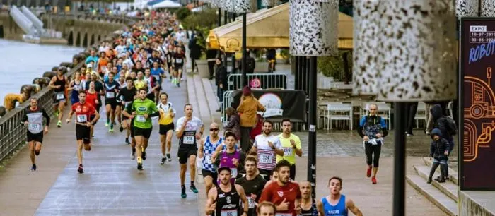 Hundreds of runners participating in a 10 km race on the Bordeaux waterfront, wearing colorful race bibs, with crowds and historic buildings in the background.