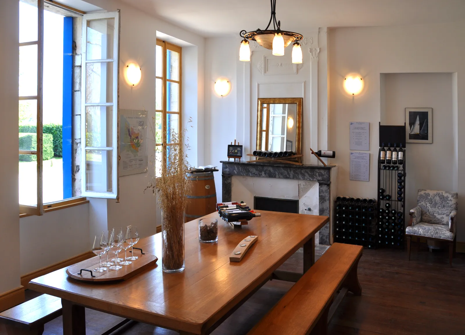 Elegant wine cellar interior featuring a wooden tasting table, wine glasses, marble fireplace, black wine storage cabinet and gilded mirror in natural light