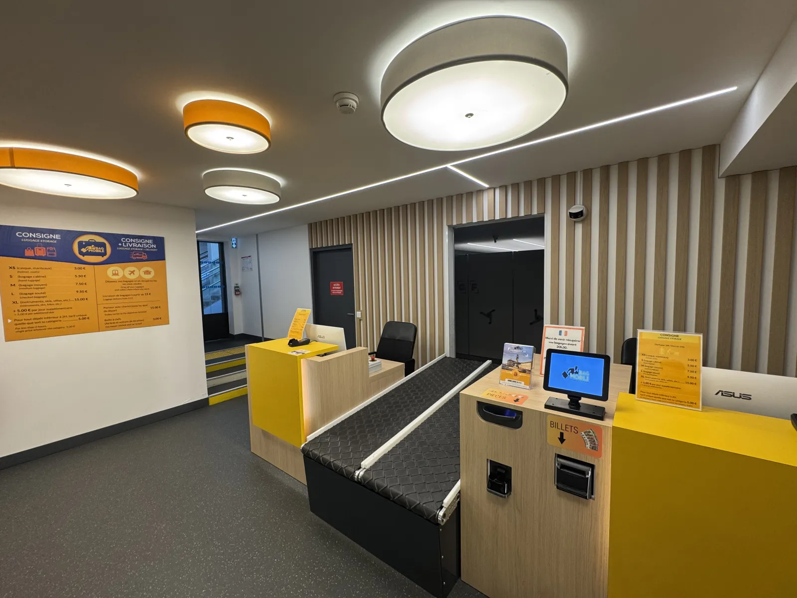 Modern interior of a Consigne Bag Mobile store in Bordeaux featuring a yellow counter, display screens, ticket dispenser, and signage offering baggage storage services.