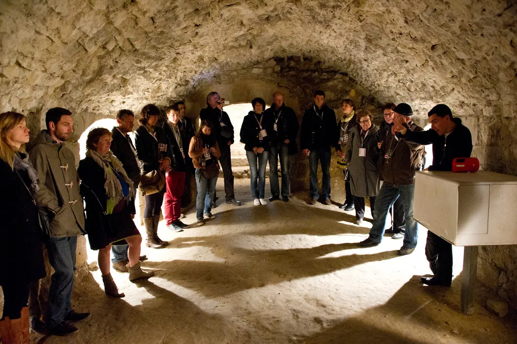Group of visitors on a guided tour through the vaulted underground passages of Blaye Citadel, lit by natural light from above.