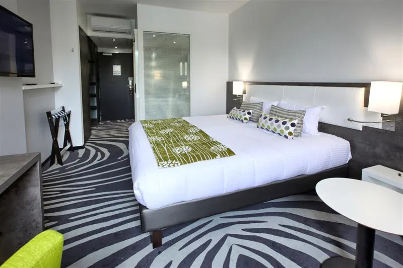 Modern hotel bedroom with double bed, white linens, geometric black and white décor, bedside lamp, and ensuite bathroom in Bordeaux