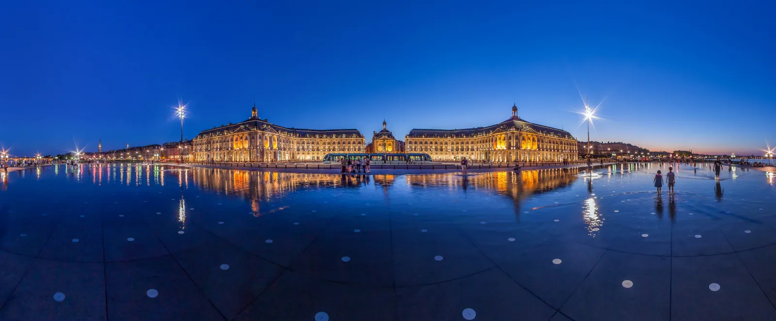 Night view of Place de la Bourse in Bordeaux with illuminated historic buildings reflected in the water mirror at twilight.
