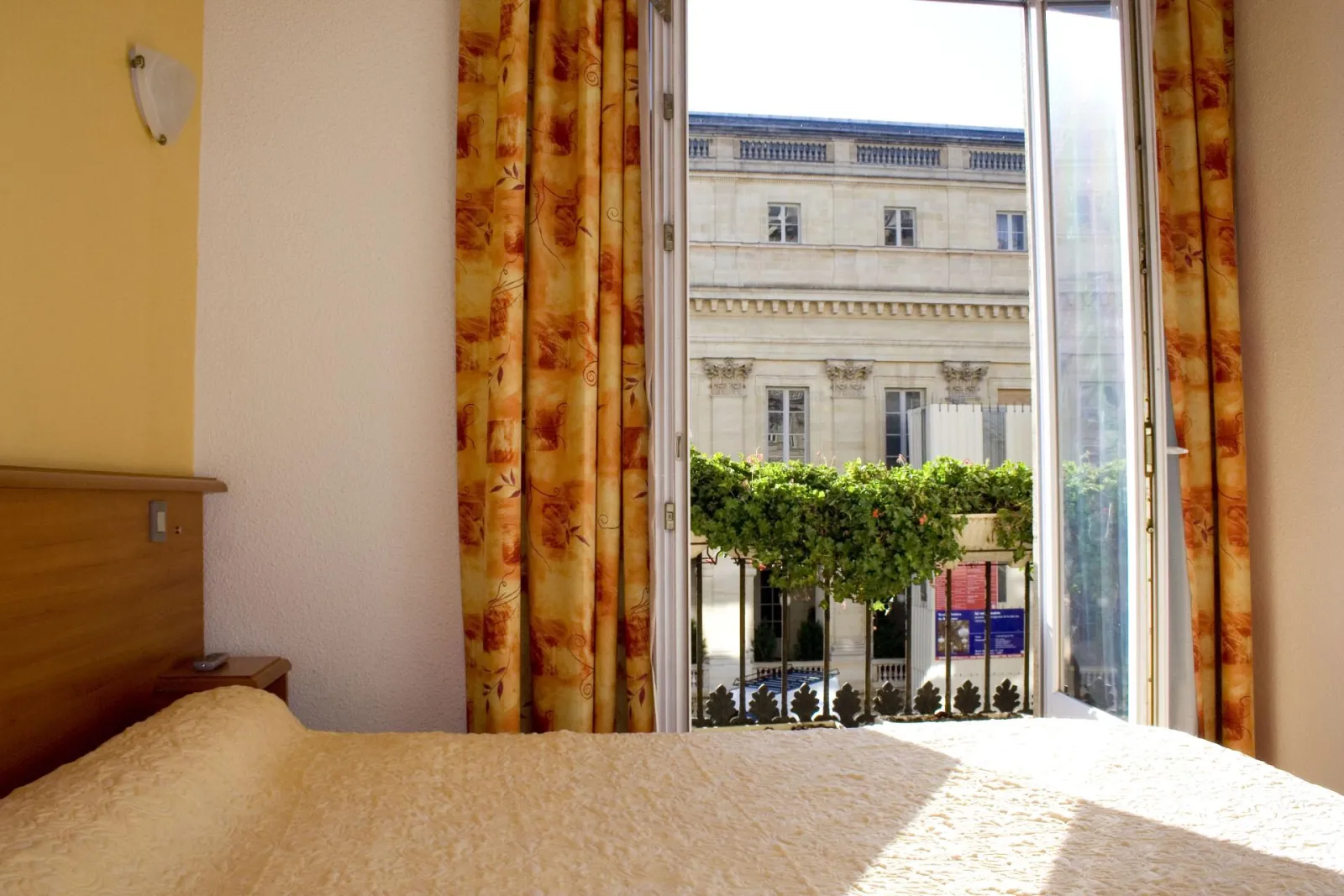 Hotel room overlooking the Bordeaux Opera House facade and interior courtyard, gold curtains, bed with beige bedspread