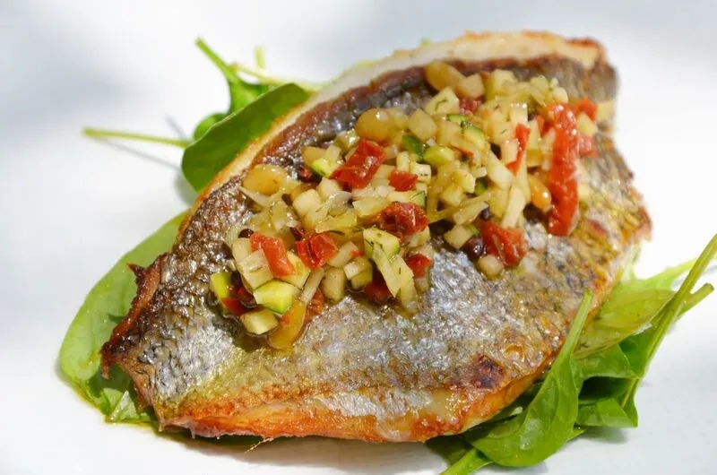 Grilled fish fillet topped with colorful diced vegetables, served on a bed of fresh arugula at a Bordeaux restaurant