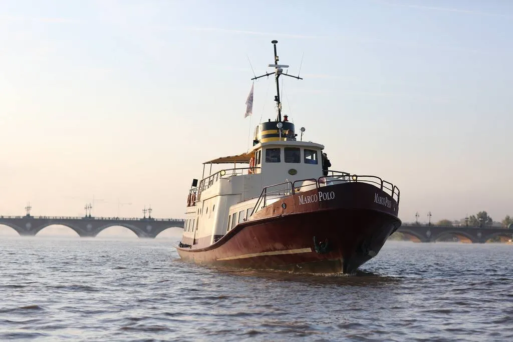 The Marco Polo ship sailing on the Garonne River in Bordeaux, with the Stone Bridge visible in the background.