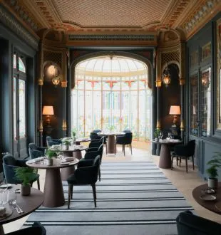 Elegant interior of Grand Barrail restaurant in Bordeaux featuring ornate gilded ceiling, arched bay window, round tables, black chairs and refined decor