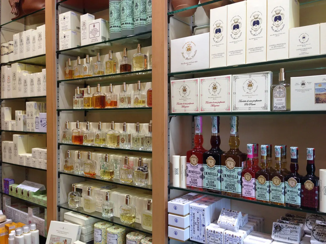 Luxury perfumery display cabinet with glass shelves showcasing perfume bottles, soap boxes, and liqueurs in an upscale Bordeaux shop.