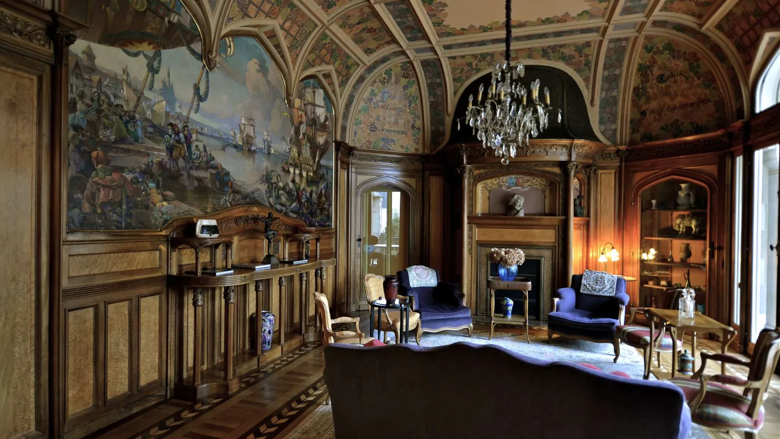 Luxurious interior of Hôtel Frugès in Bordeaux featuring decorated coffered ceiling, large historical painting, period furniture, crystal chandeliers and refined wood paneling.