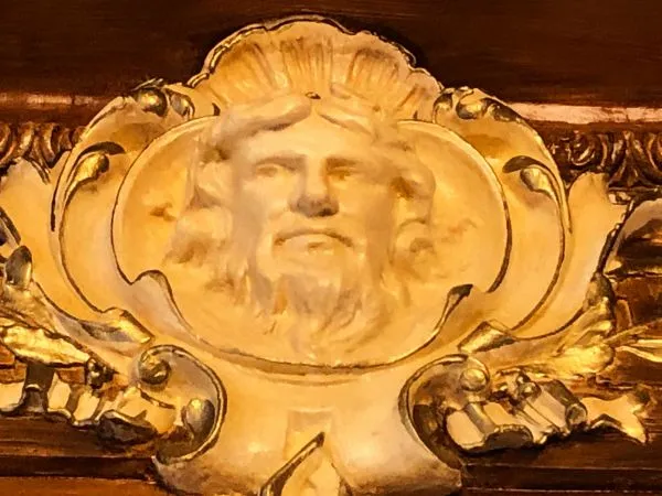 Gilded architectural ornament featuring a bearded face mask surrounded by rococo scrollwork details