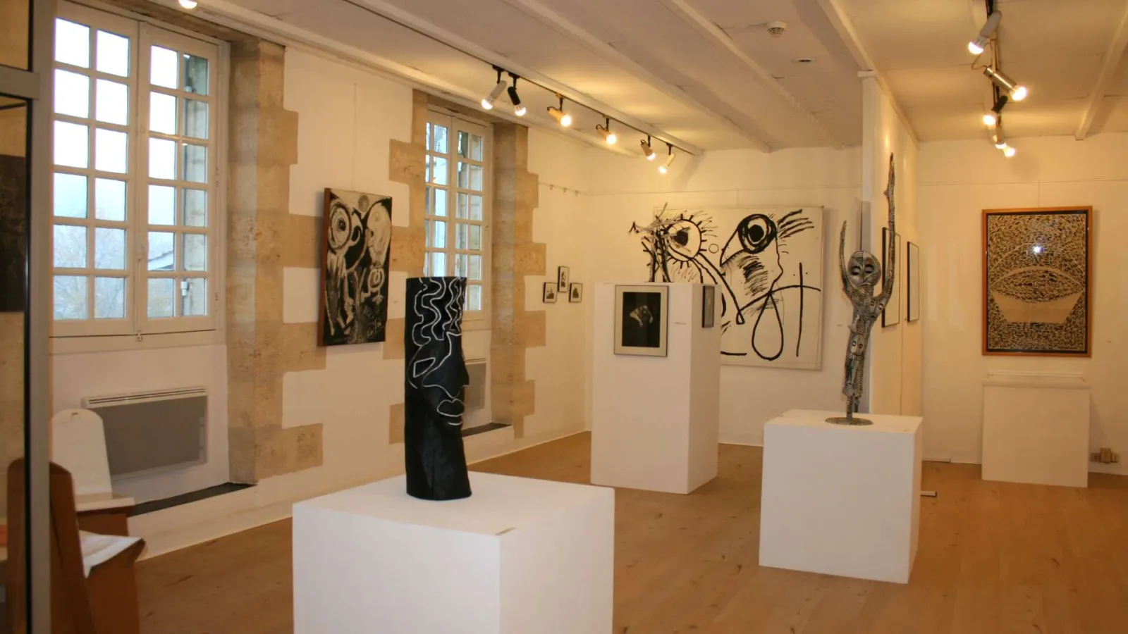 Interior of the Museum of Free Creation in Bordeaux displaying abstract sculptures and drawings on white walls and pedestals, with large windows and track lighting.