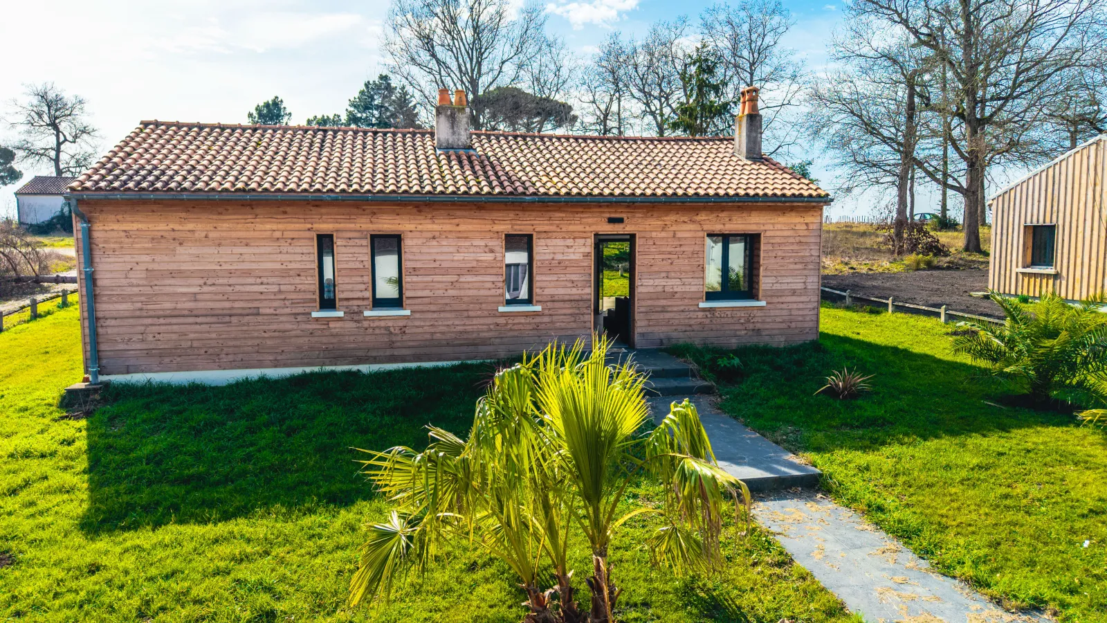 Wooden eco-cottage with tiled roof surrounded by green lawn and paved pathway, located at Château Loudenne near Bordeaux