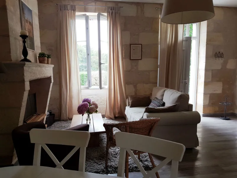 Elegant living room at Maison des Hôtesses in Bordeaux featuring a fireplace, gray armchairs, tall glass doors, beige curtains and classic decor