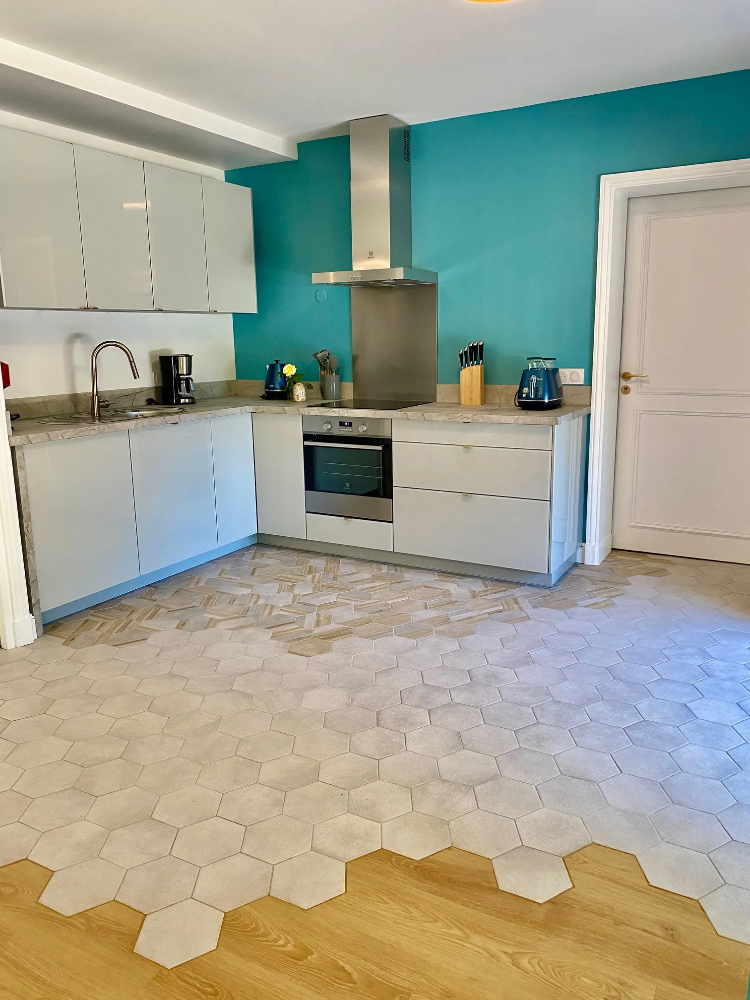 Modern kitchen with turquoise walls, white cabinets, gray countertop, white hexagonal tiles and wooden flooring in Bordeaux at La Maison L'Eperon
