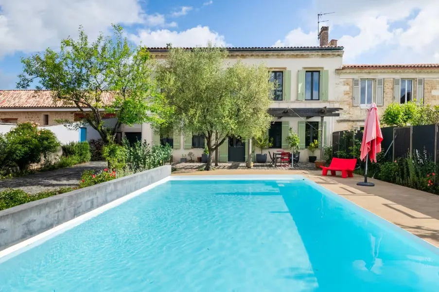 Charming stone house with rectangular turquoise swimming pool, paved terrace, olive trees, red umbrella and traditional architecture near Bordeaux