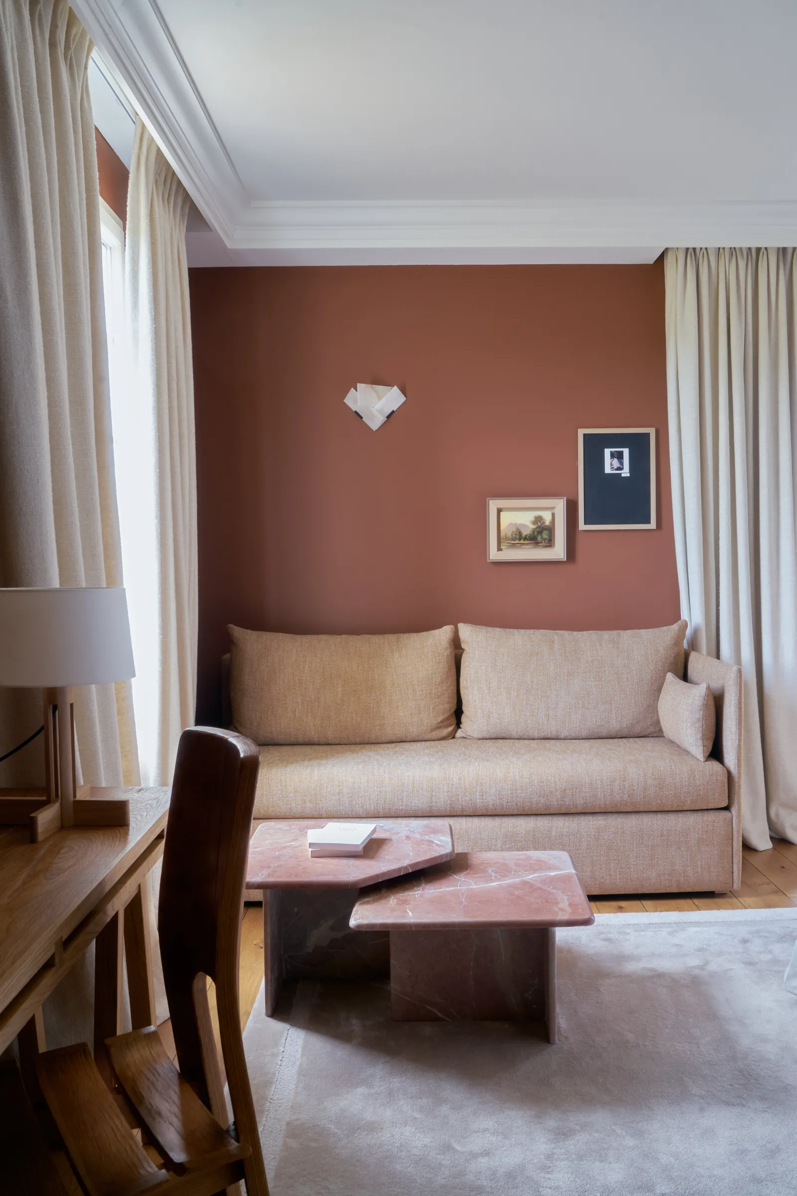 Elegant living room with terracotta walls, light beige sofa, dusty pink coffee table, cream curtains and framed artworks, filled with natural light.