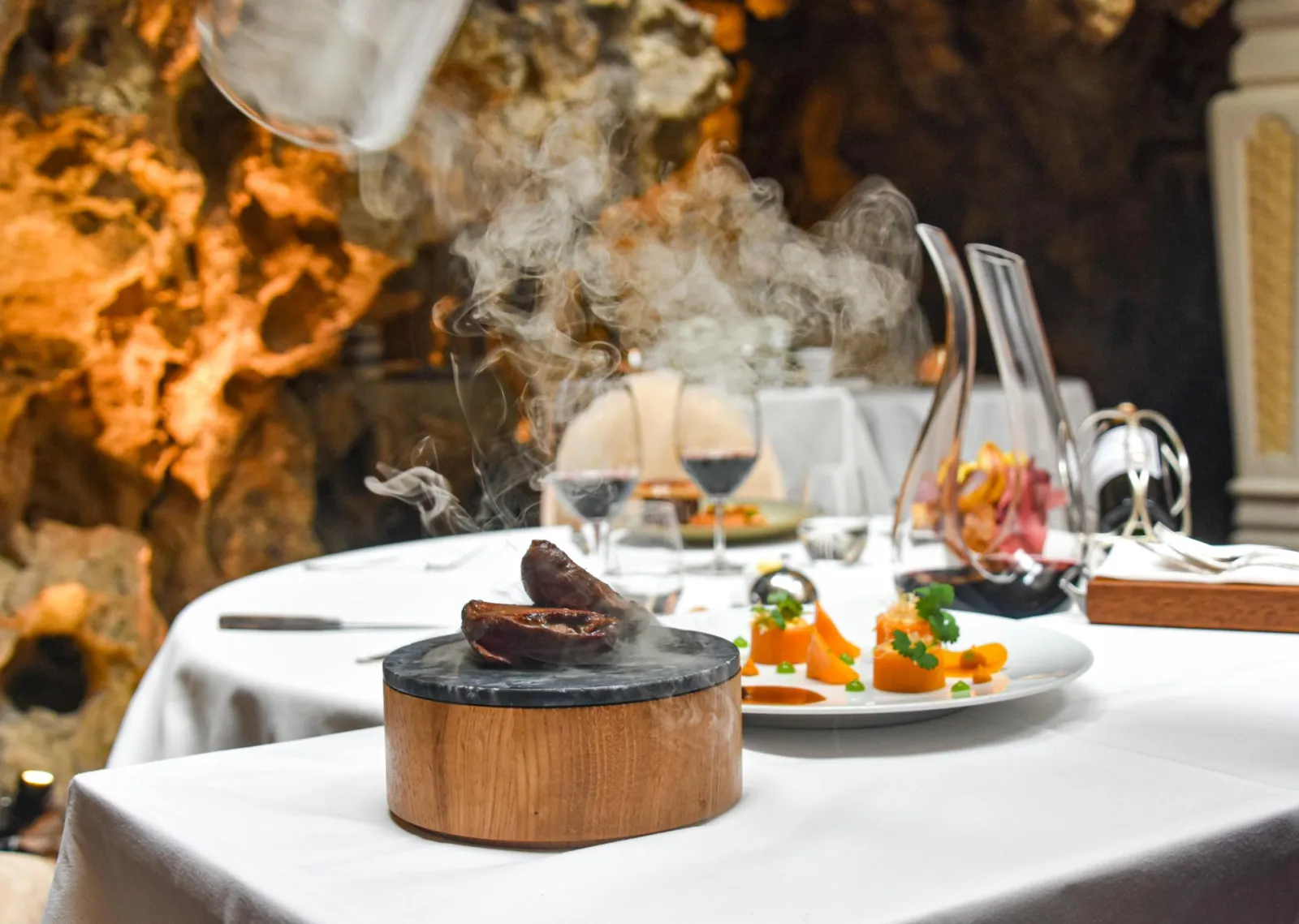 Elegant dining table at Chapon Fin restaurant in Bordeaux featuring a smoking dish in a wooden and slate box, accompanied by refined cuisine and wine glasses