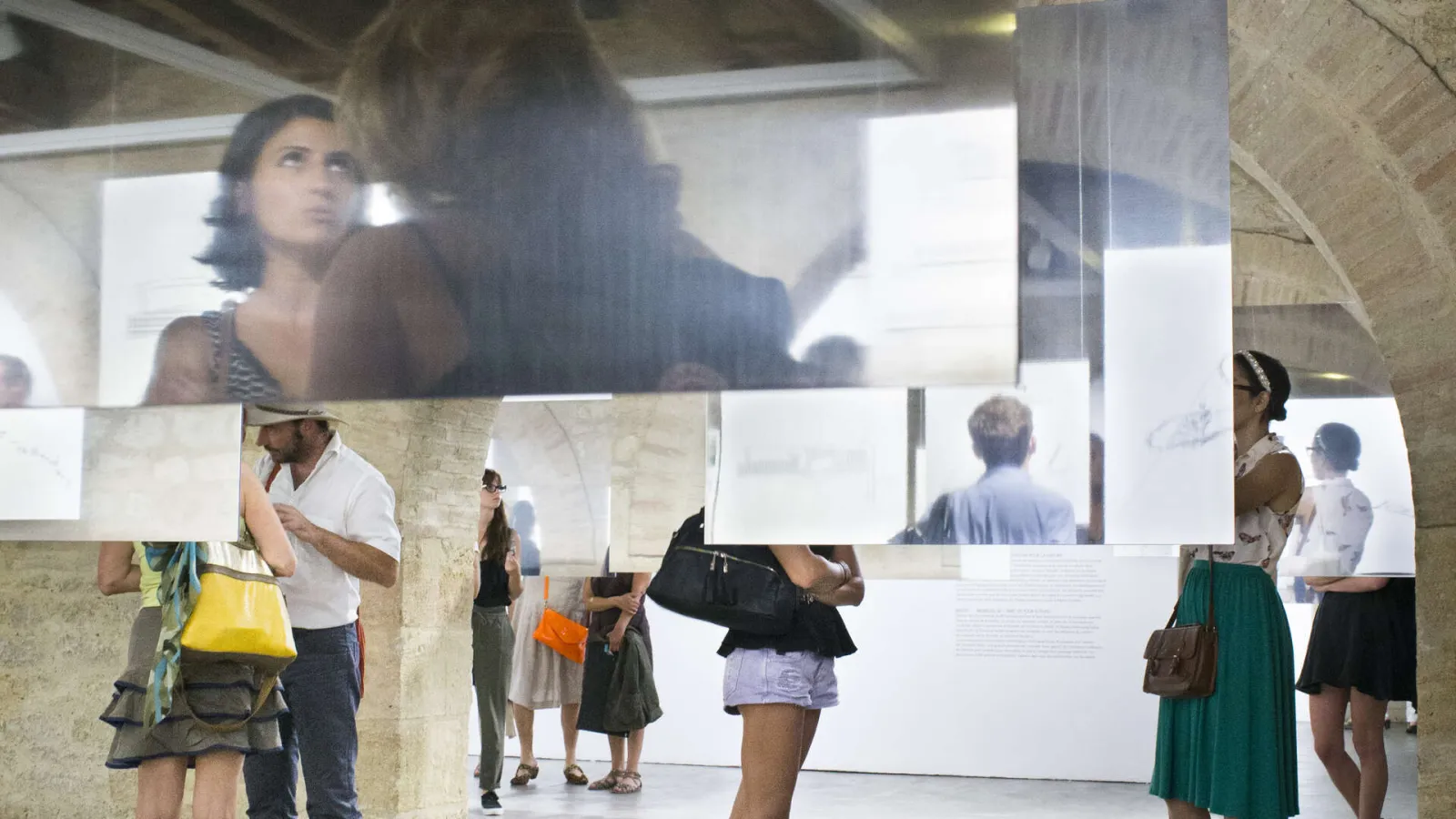 Visitors viewing an architectural exhibition with information panels and projection screen in a contemporary space at Arc en rêve architecture center in Bordeaux.