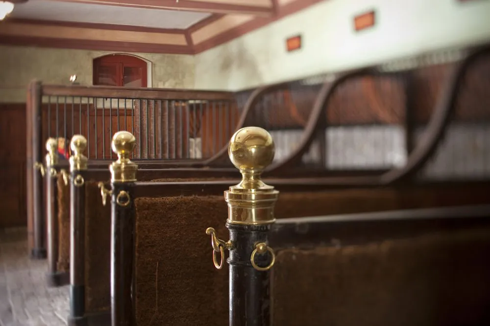 Interior of the Horse Museum in Bordeaux displaying traditional wooden horse stalls with brass fittings and equestrian tack, showcasing classic stable equipment.