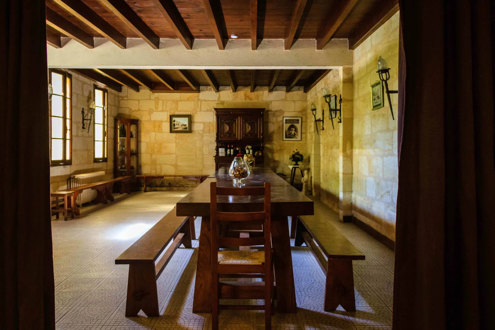 Rustic dining room at Château Champion in Bordeaux, featuring a wooden table with benches, exposed ceiling beams, pale stone walls, and period furniture
