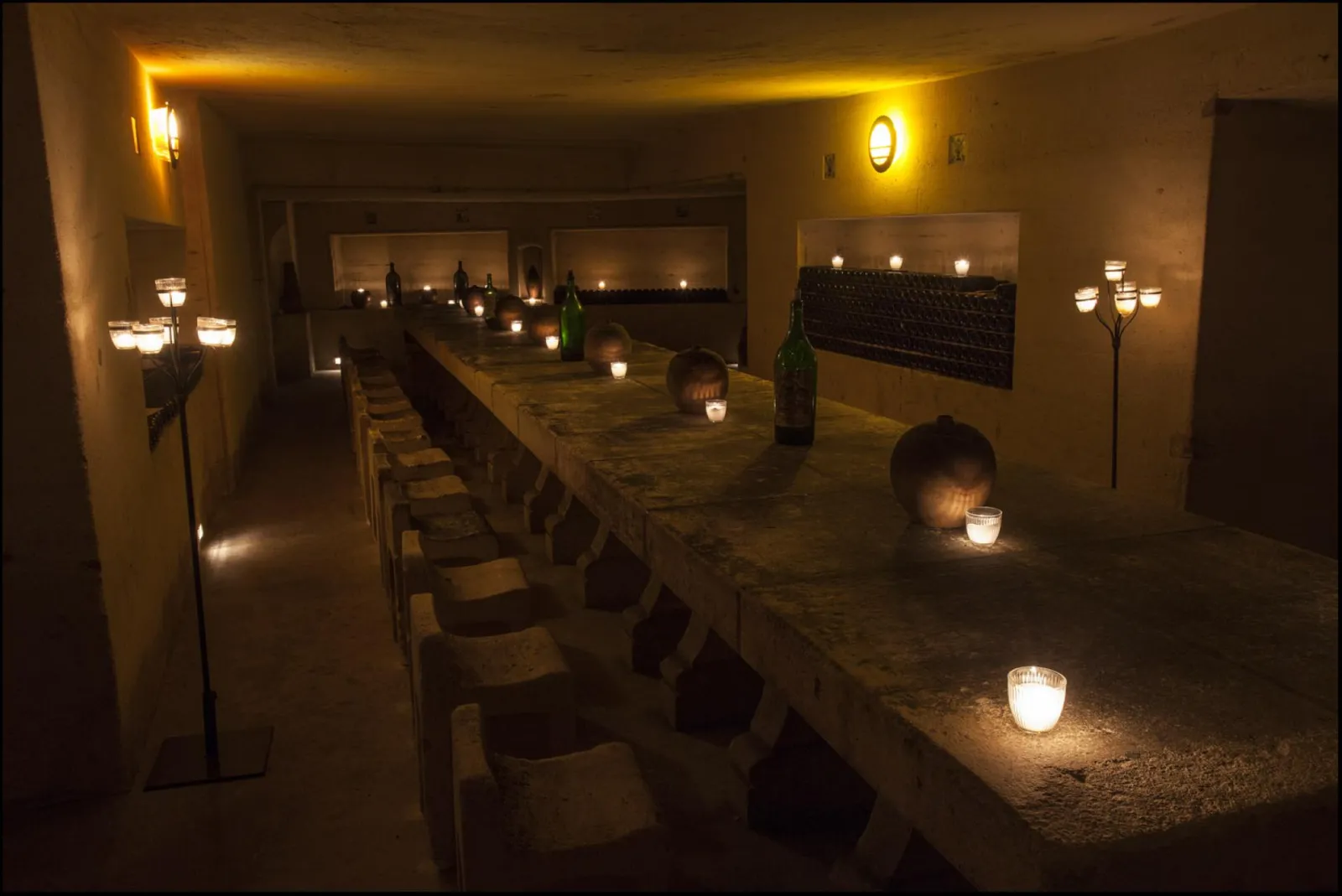 Underground chamber of Château de La Rivière in Bordeaux, lit by candlelight and wall sconces, featuring a long stone table and black chairs