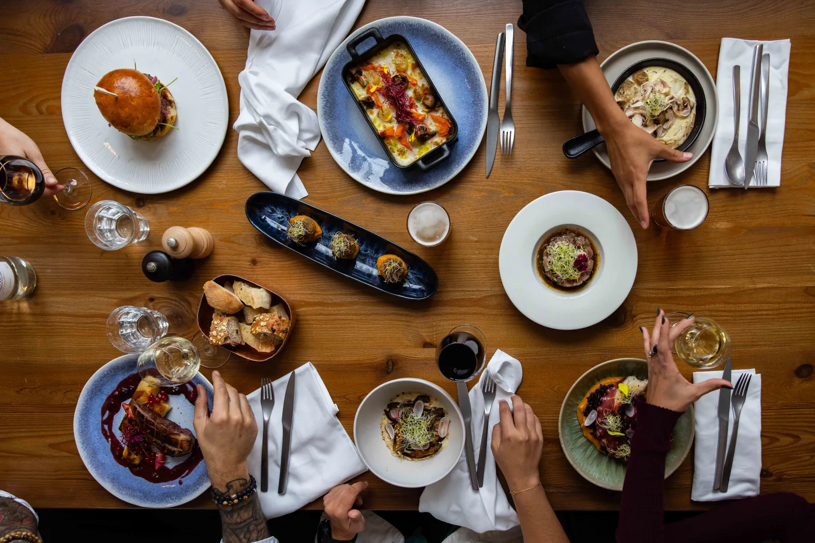 Overhead view of a restaurant table with multiple diners enjoying various gourmet dishes accompanied by white wine glasses in a shared dining experience at Bistrot Le Saint-Jean in Bordeaux.