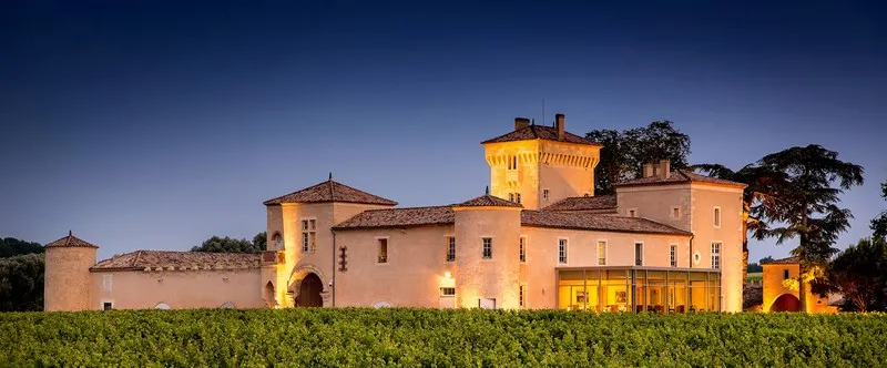 Château Lafaurie Peyraguey lit up at dusk, Renaissance-style ochre-colored castle with towers and vineyards in foreground, Bordeaux region