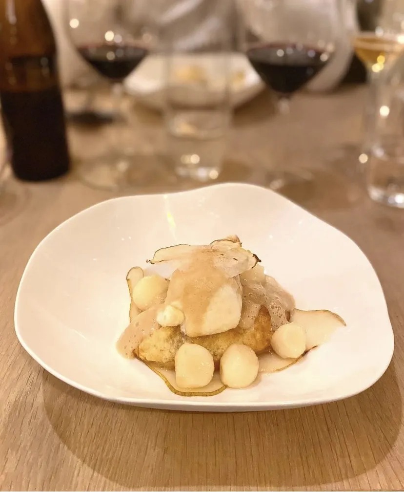 Gourmet plate featuring white meat garnished with fresh white grapes, served in an upscale Bordeaux restaurant with red wine glasses visible in the background.