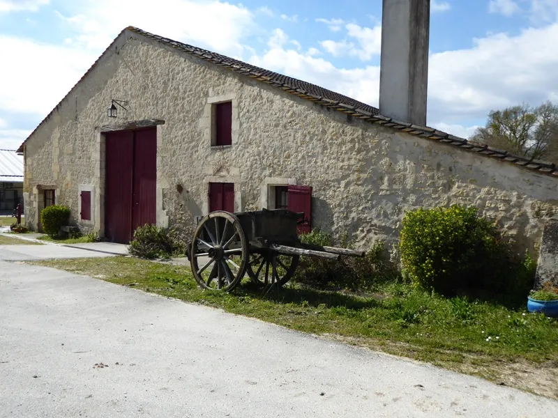 Stone building with burgundy doors and windows, wooden-wheeled cart in front of the facade, chimney in the background, Château de Lisennes near Bordeaux