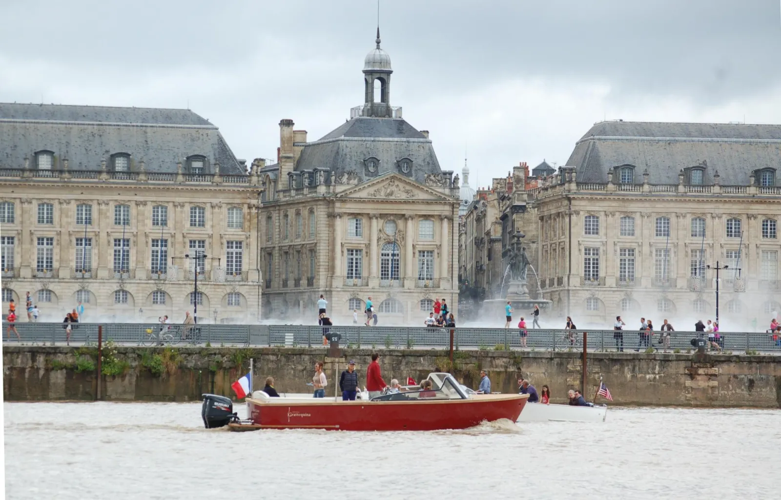 The red Grattequina water taxi boat on the Garonne River in Bordeaux, in front of Place de la Bourse and its 18th-century classical buildings with water mirror.