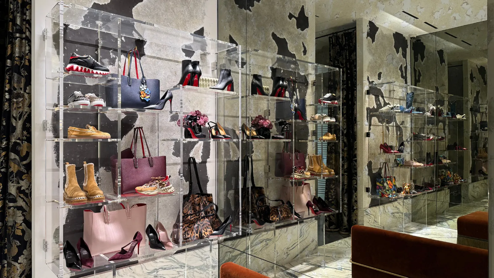 Luxury fashion boutique window display in Bordeaux showcasing high-end shoes, handbags, and accessories arranged on illuminated glass shelves with black leaf wall decoration.