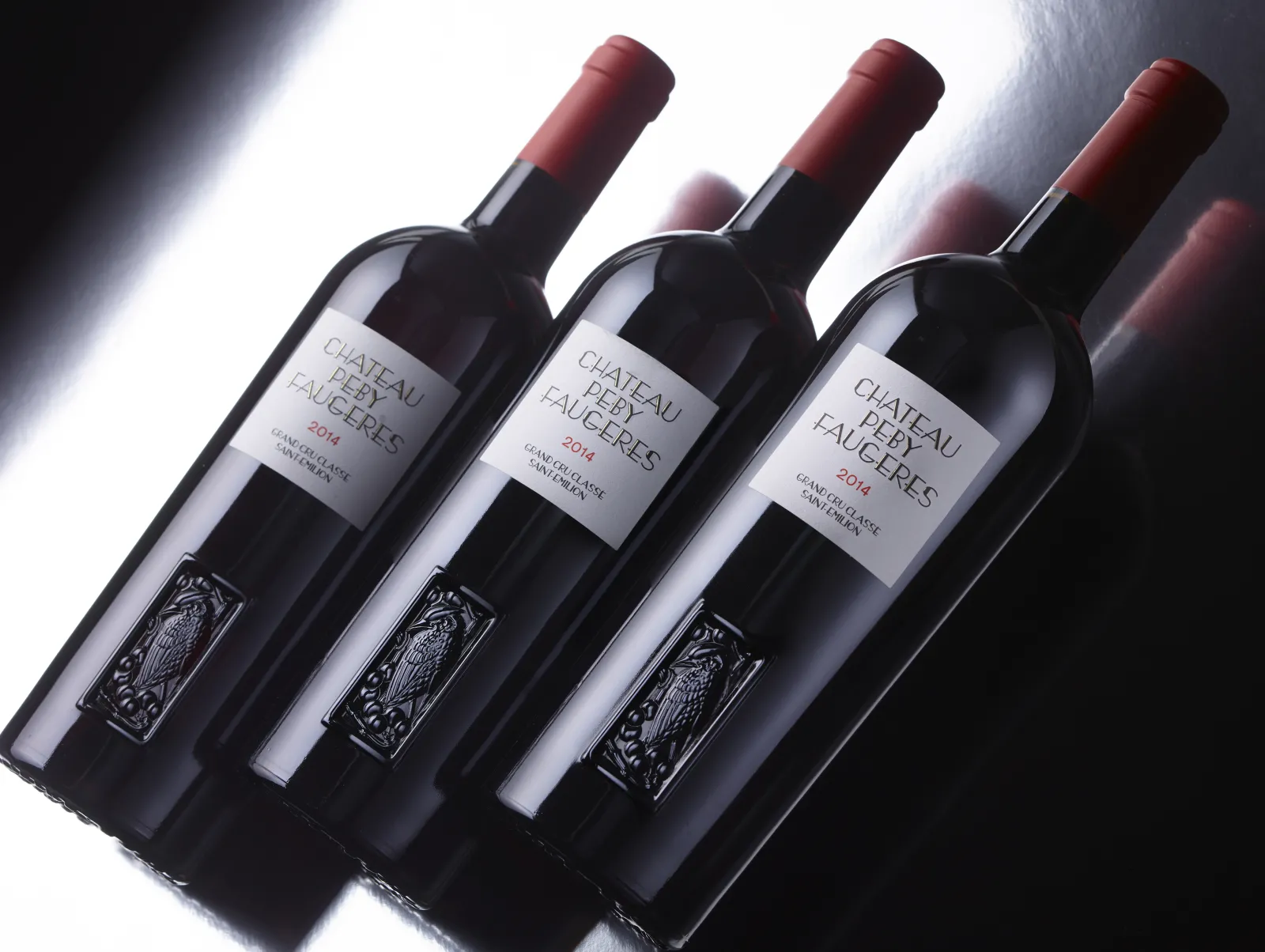 Three bottles of red wine Château Peby Faugères vintage 2014 from Bordeaux, displayed side by side with white labels and burgundy capsules.
