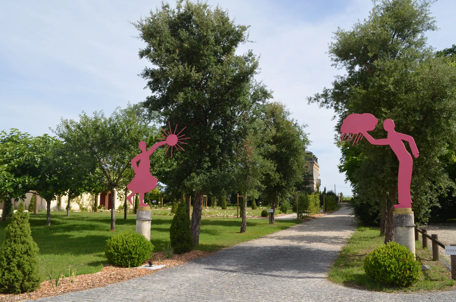 Park pathway with two bright pink sculptural figures playing, surrounded by trees and green spaces at Château Yon-Figeac in Bordeaux.