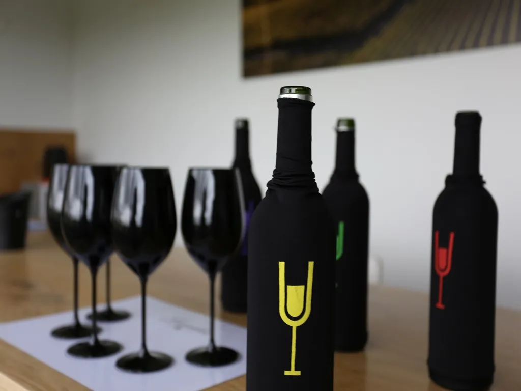 Black wine bottles with colorful glass-shaped labels displayed with empty black wine glasses on a white table in a minimalist interior setting.
