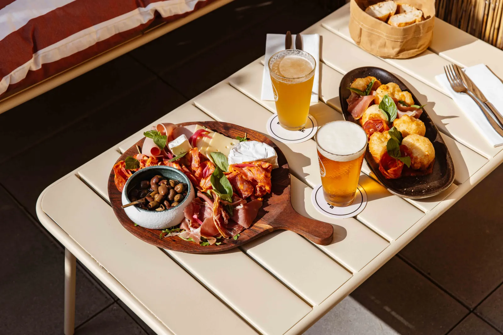 Restaurant table featuring a wooden board with cured meats and cheese, a skillet of roasted potatoes and meats, and glasses of light beer in an upscale setting at Lago Bordeaux