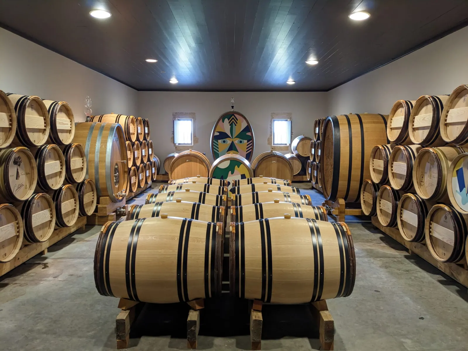 Barrel aging cellar at Château La Rose Perrière in Bordeaux featuring symmetrically arranged oak barrels and wooden casks in the foreground