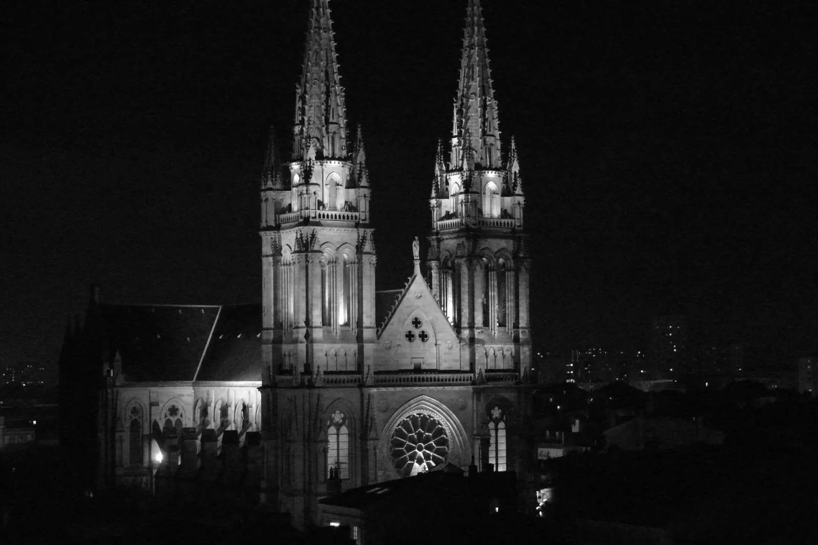 Night view of the illuminated Saint-Louis Church in Bordeaux, featuring two tall Gothic spires and a central rose window