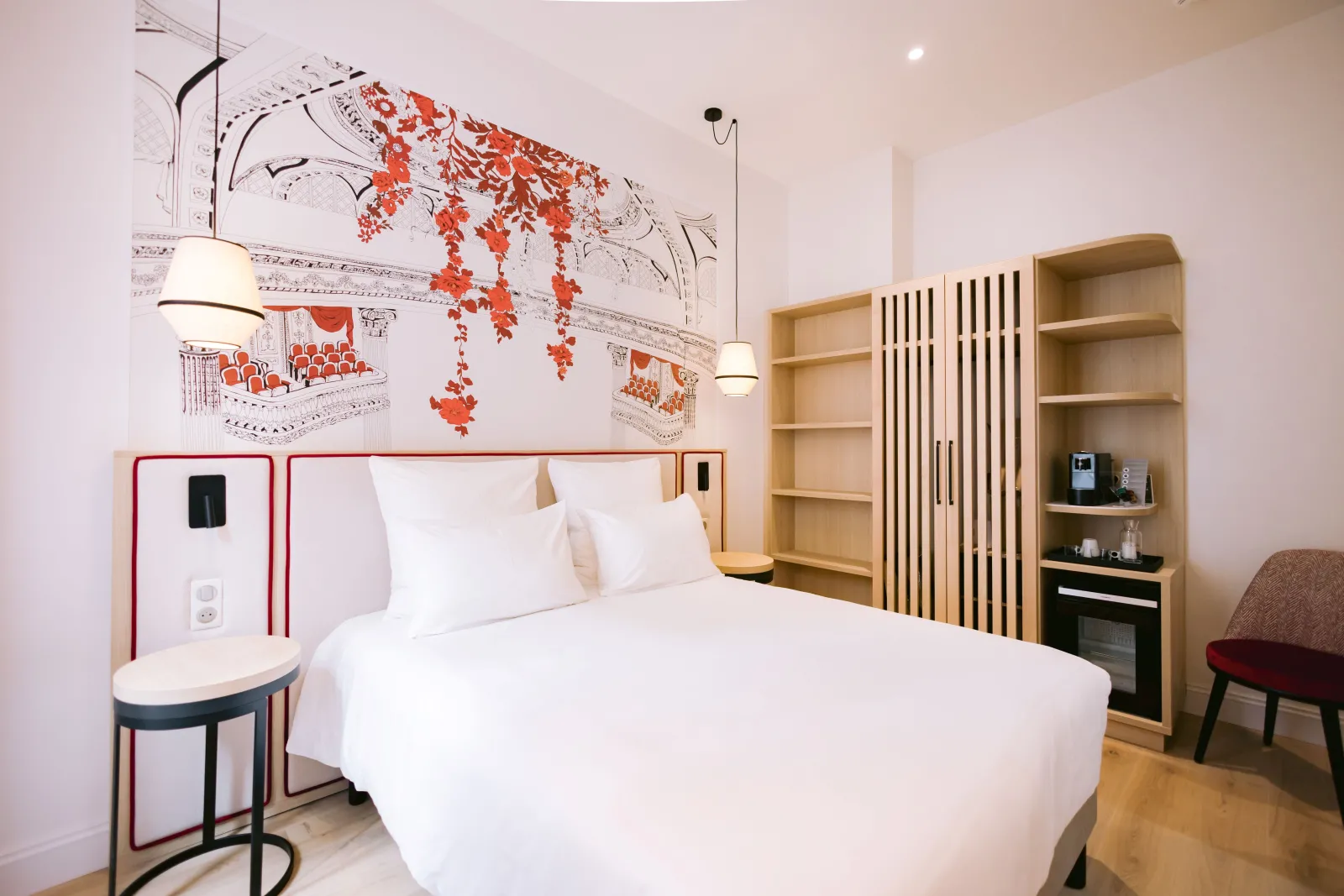 Modern hotel room with white bed, white walls, red and white wall decorative pattern, light wood furniture, and built-in shelving at Majestic Hotel Bordeaux