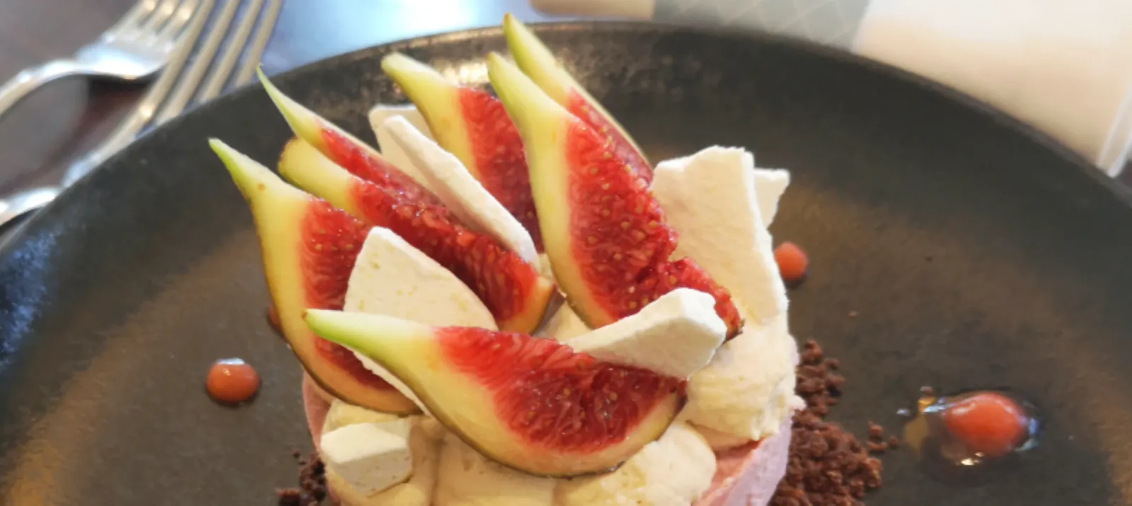 Fine dining dessert plate from Comptoir de Sèze in Bordeaux featuring fresh sliced figs, white mousse, cocoa powder, and red sauce pearls artfully arranged on a dark plate.